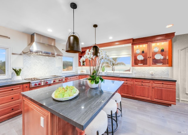 kitchen with wall chimney exhaust hood, a kitchen island, hanging light fixtures, and stainless steel gas cooktop