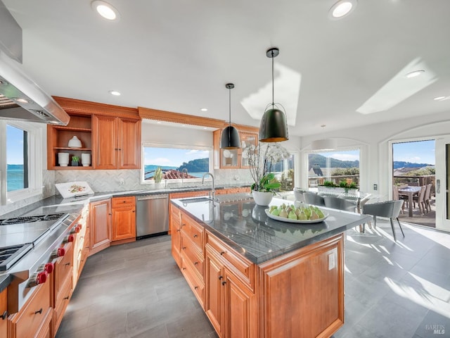 kitchen featuring appliances with stainless steel finishes, ventilation hood, sink, decorative light fixtures, and a water view