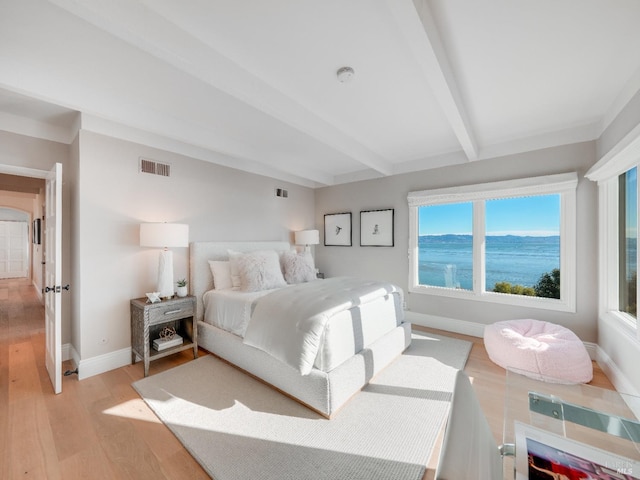 bedroom with beam ceiling, a water view, light hardwood / wood-style floors, and multiple windows