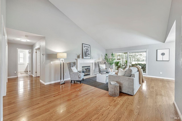 living room with a tiled fireplace, high vaulted ceiling, and light hardwood / wood-style flooring