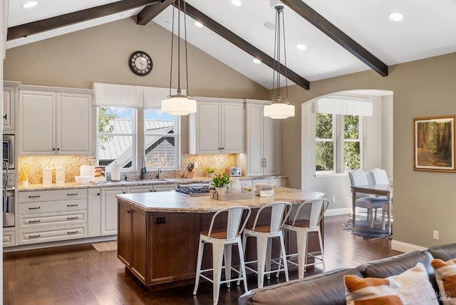 kitchen featuring a breakfast bar area, light stone countertops, white cabinets, a kitchen island, and decorative light fixtures