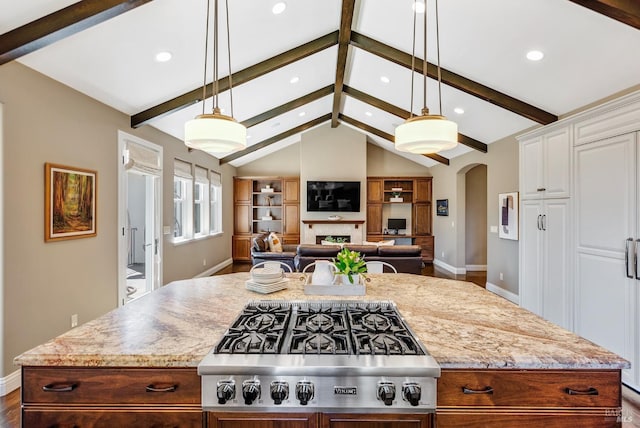 kitchen with a center island, light stone counters, lofted ceiling with beams, stainless steel gas cooktop, and decorative light fixtures