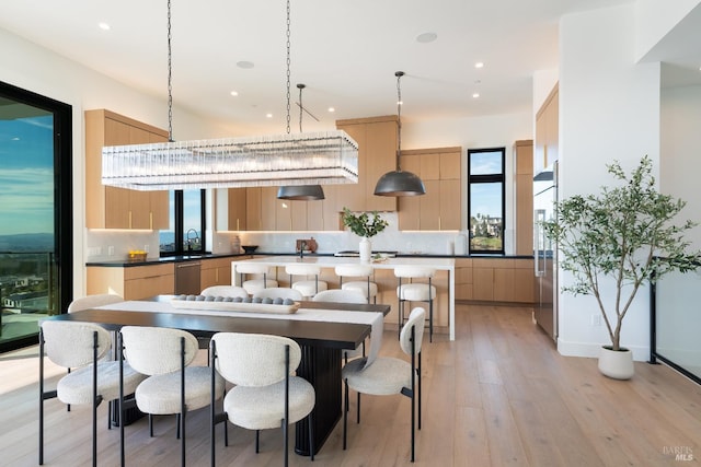 kitchen with backsplash, light brown cabinetry, hanging light fixtures, and light hardwood / wood-style flooring