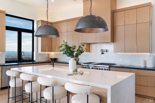 kitchen with pendant lighting, a kitchen island with sink, stainless steel dishwasher, dark stone countertops, and light wood-type flooring