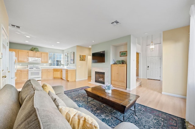 living room with light wood-type flooring, a tiled fireplace, and sink