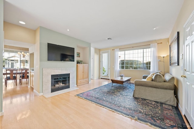 living room featuring a tile fireplace, a chandelier, and light hardwood / wood-style flooring