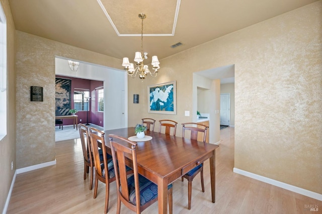 dining space featuring a tray ceiling, a chandelier, and light hardwood / wood-style flooring