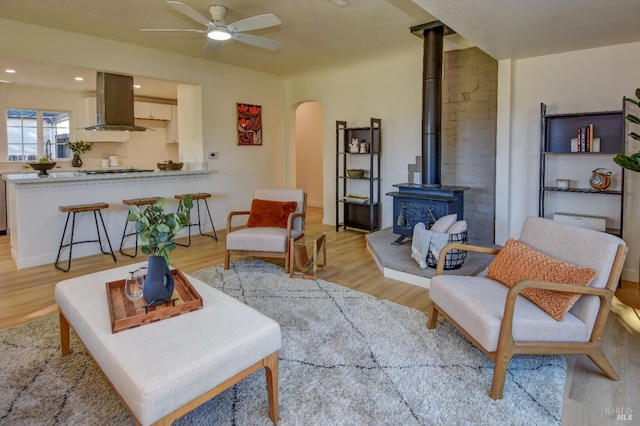 living room featuring light hardwood / wood-style floors, a wood stove, and ceiling fan