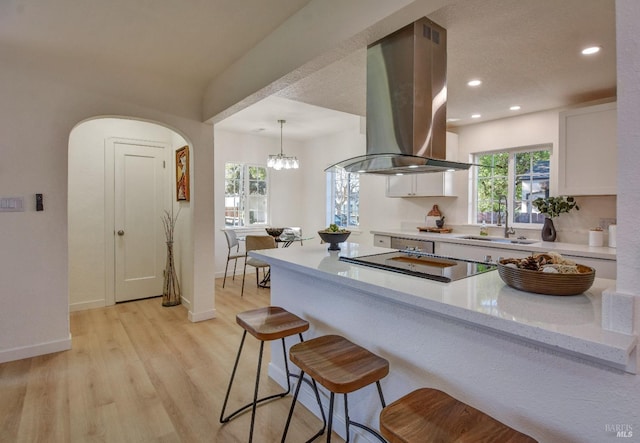 kitchen featuring sink, island exhaust hood, white cabinetry, hanging light fixtures, and black electric cooktop