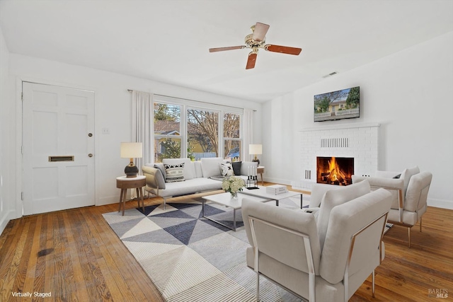 living room with ceiling fan, wood-type flooring, and a brick fireplace