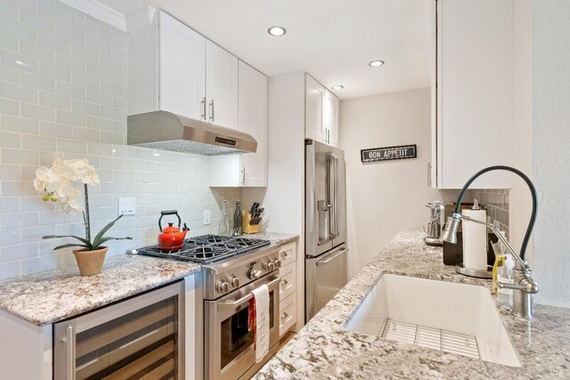 kitchen featuring high quality appliances, light stone counters, beverage cooler, decorative backsplash, and under cabinet range hood