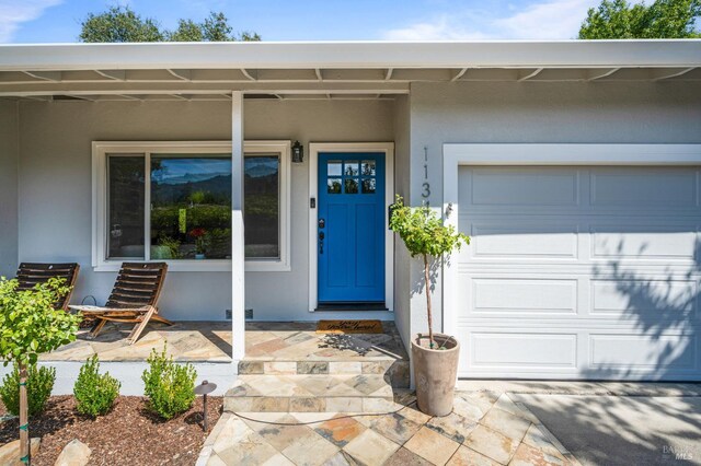 doorway to property with a garage, stucco siding, and a porch