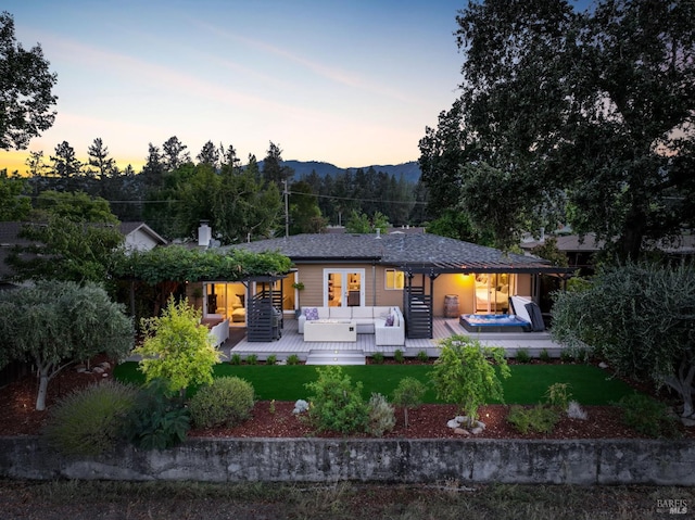 back of house at dusk with a deck with mountain view, a lawn, and an outdoor living space