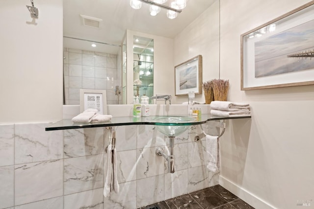 bathroom featuring marble finish floor, tiled shower, a sink, and tile walls