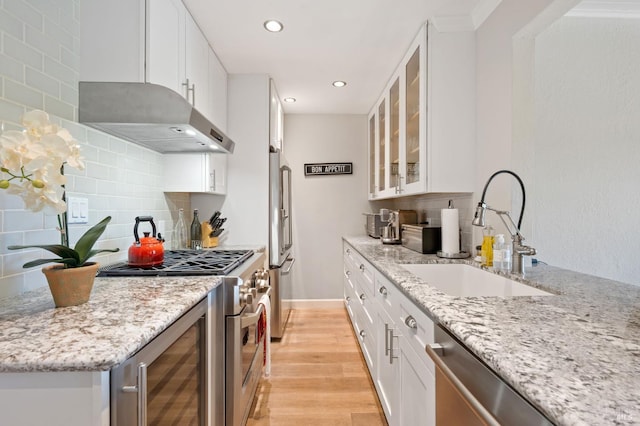 kitchen with high end appliances, light wood-style flooring, light stone counters, under cabinet range hood, and a sink