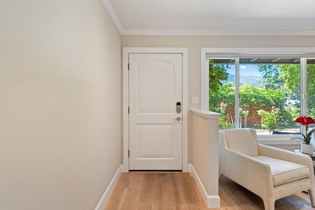 doorway to outside featuring baseboards, ornamental molding, and light wood finished floors