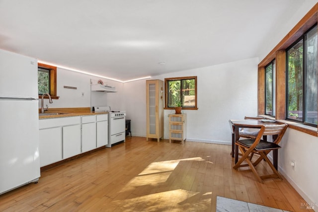 kitchen with white appliances, under cabinet range hood, a sink, and light wood-type flooring
