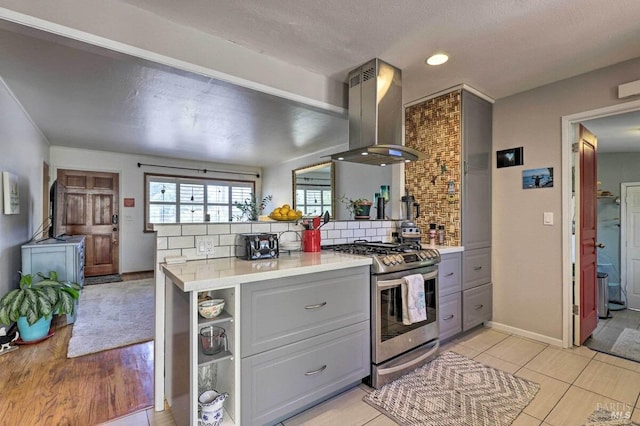 kitchen featuring gray cabinetry, island exhaust hood, tasteful backsplash, and stainless steel gas stove