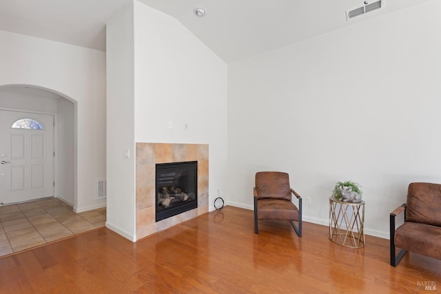 unfurnished room featuring hardwood / wood-style flooring, a tile fireplace, and lofted ceiling