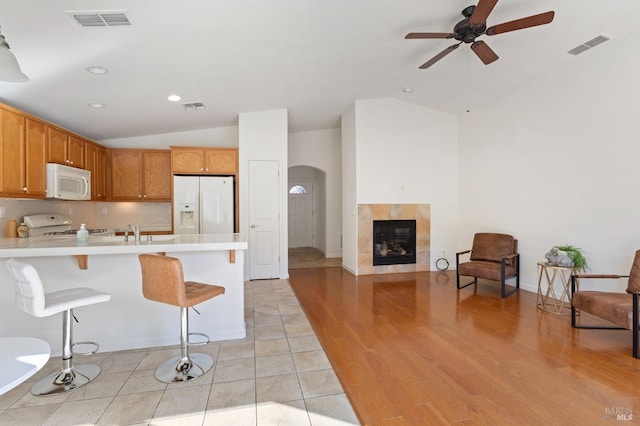 kitchen featuring vaulted ceiling, light hardwood / wood-style floors, white appliances, a tiled fireplace, and a breakfast bar area