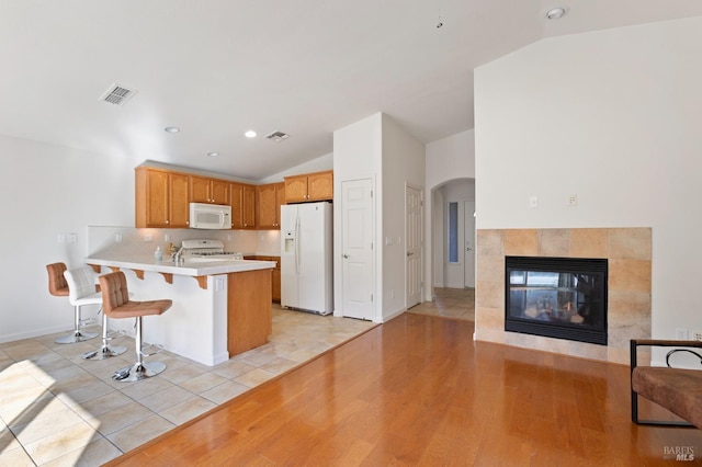 kitchen with kitchen peninsula, vaulted ceiling, white appliances, and a breakfast bar area