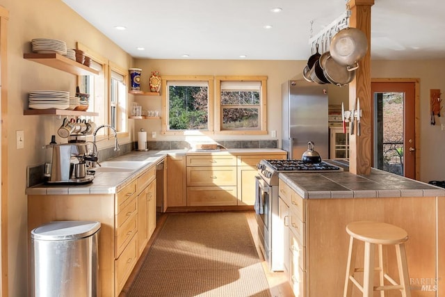 kitchen featuring a wealth of natural light, stainless steel appliances, light brown cabinetry, sink, and tile countertops