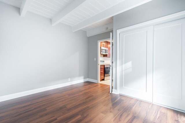 unfurnished bedroom featuring dark wood-type flooring, beam ceiling, and a closet