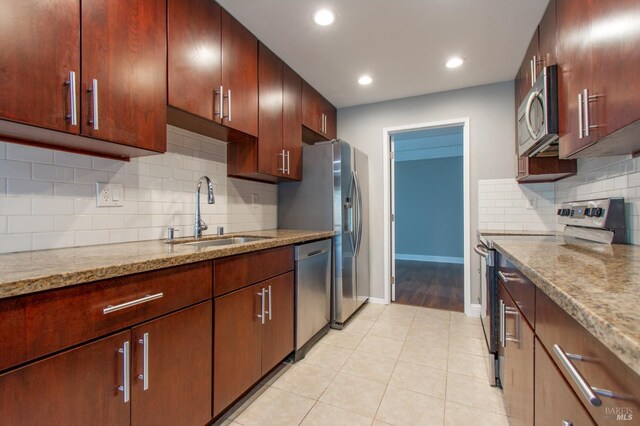 kitchen with light tile patterned flooring, sink, light stone counters, appliances with stainless steel finishes, and decorative backsplash