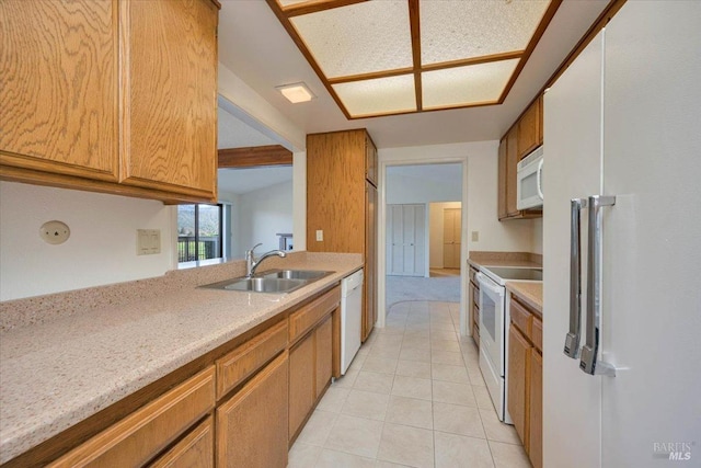 kitchen with light tile patterned floors, white appliances, brown cabinetry, and a sink