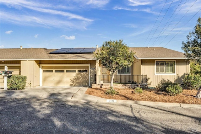 single story home featuring a shingled roof, roof mounted solar panels, driveway, and an attached garage