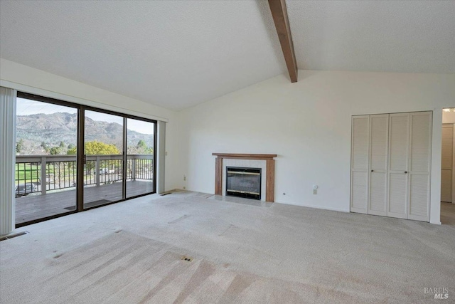 unfurnished living room featuring vaulted ceiling with beams, a textured ceiling, a mountain view, carpet floors, and a tiled fireplace