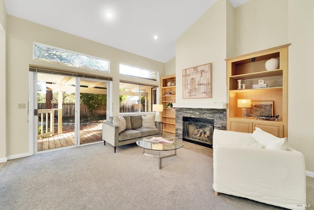 living room featuring carpet flooring, built in shelves, high vaulted ceiling, and a stone fireplace