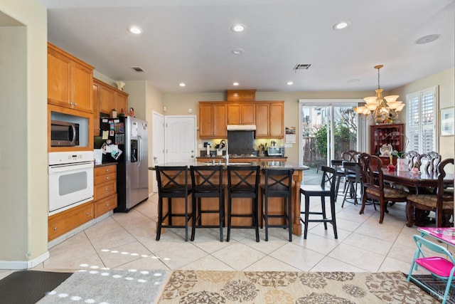 kitchen featuring stainless steel appliances, hanging light fixtures, a center island with sink, and light tile patterned floors