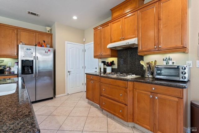 kitchen with white gas cooktop, stainless steel fridge with ice dispenser, light tile patterned floors, dark stone countertops, and decorative backsplash