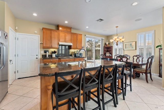 kitchen featuring pendant lighting, sink, dark stone countertops, a center island with sink, and light tile patterned flooring