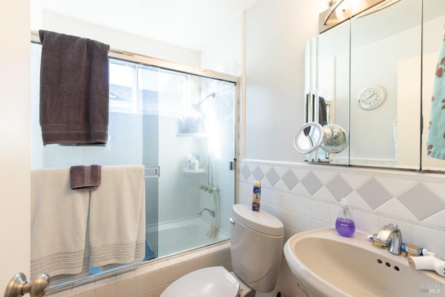 bathroom with sink, a shower with shower door, tile walls, and toilet