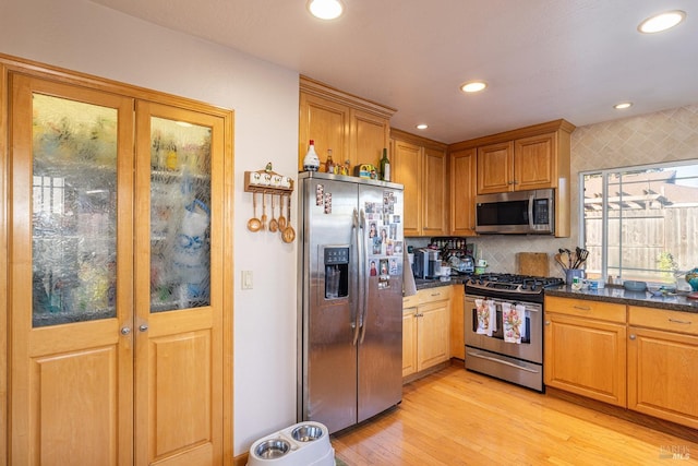 kitchen featuring decorative backsplash, light hardwood / wood-style flooring, dark stone counters, and appliances with stainless steel finishes