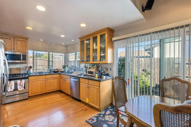 kitchen with sink, light hardwood / wood-style flooring, dark stone countertops, appliances with stainless steel finishes, and tasteful backsplash