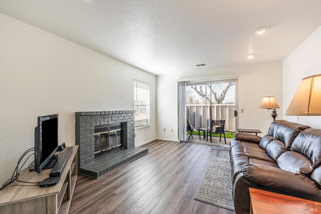 living area featuring a textured ceiling, wood finished floors, visible vents, baseboards, and a brick fireplace