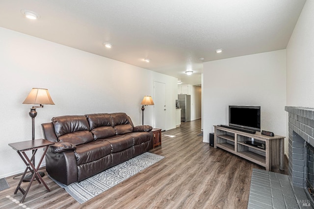 living area featuring a brick fireplace, a textured ceiling, baseboards, and wood finished floors