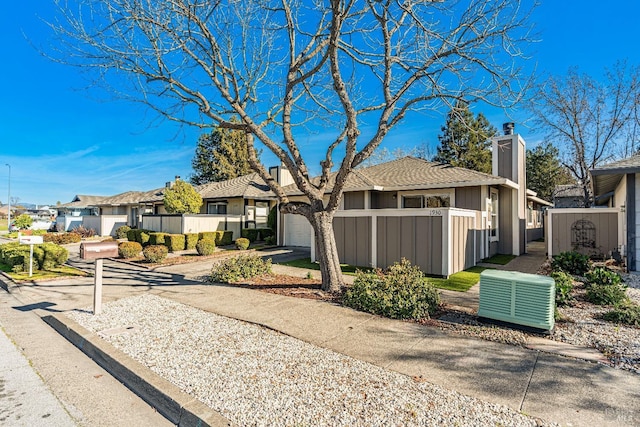 view of front of house featuring a fenced front yard, central air condition unit, concrete driveway, an attached garage, and a residential view