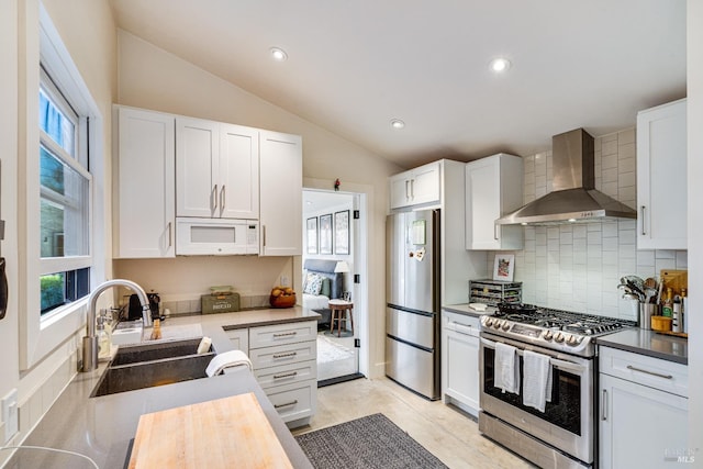 kitchen with appliances with stainless steel finishes, white cabinetry, a sink, wall chimney range hood, and butcher block countertops