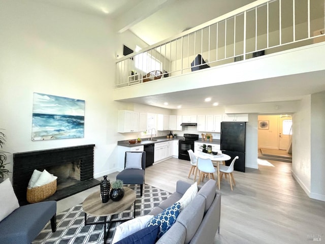 living area featuring light wood-type flooring, a fireplace with raised hearth, beamed ceiling, and baseboards