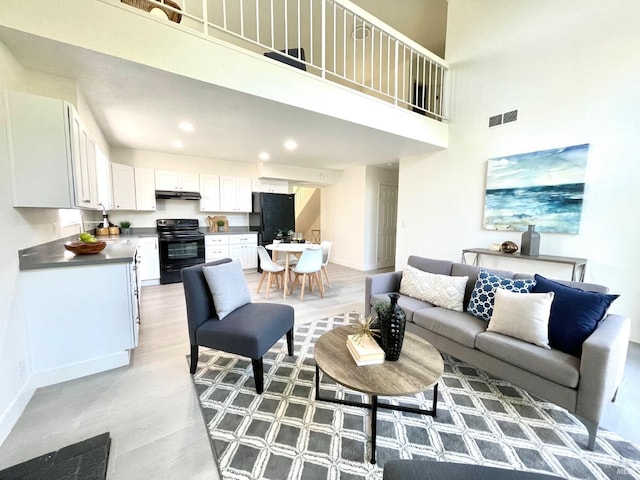 living room with baseboards, visible vents, a high ceiling, light wood-type flooring, and recessed lighting