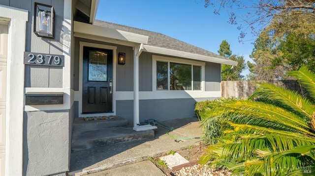 view of exterior entry with fence and roof with shingles