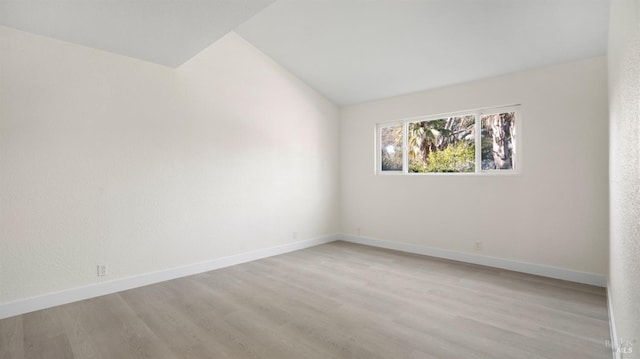 spare room with baseboards, lofted ceiling, and light wood-style floors