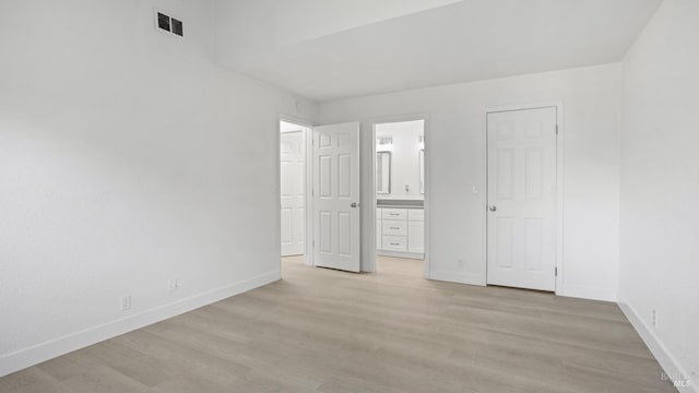 unfurnished bedroom with ensuite bath, light wood finished floors, baseboards, and visible vents