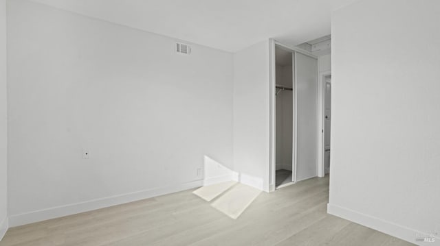 unfurnished bedroom featuring visible vents, baseboards, light wood-style flooring, a walk in closet, and a closet