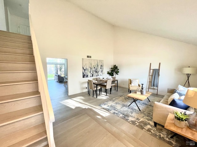 living room with baseboards, visible vents, wood finished floors, stairs, and high vaulted ceiling