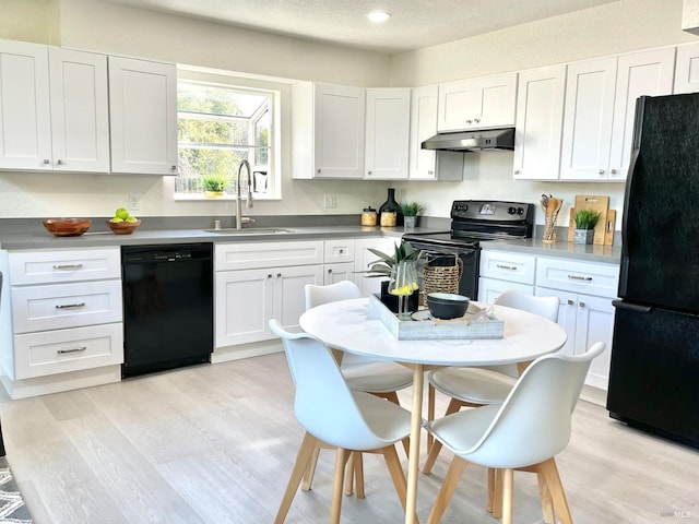 kitchen featuring light wood-style floors, under cabinet range hood, black appliances, white cabinetry, and a sink